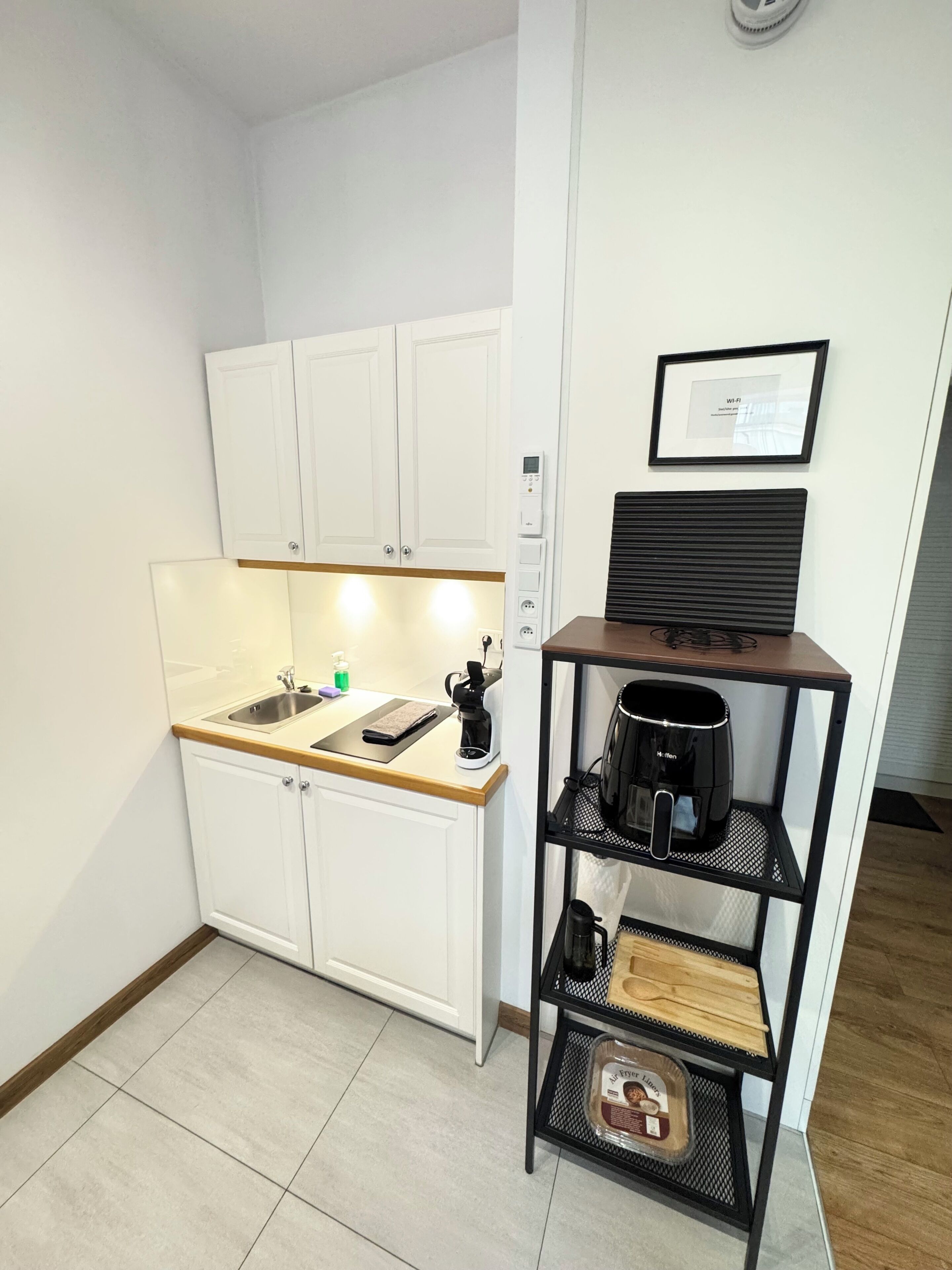 A compact kitchen with white cabinets, a coffee machine, a small shelf with a coffee maker, and a framed Wi-Fi sign.