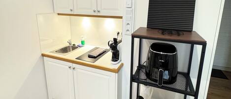 A compact kitchen with white cabinets, a coffee machine, a small shelf with a coffee maker, and a framed Wi-Fi sign.