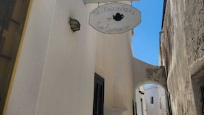 Una calle estrecha con edificios blancos, un letrero con texto griego y un cielo azul despejado.