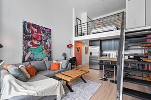 A modern apartment with a loft-style kitchen, a dining area, and a living room with a large painting. - The Eclectic - Open Concept Loft Apartment (Vancouver)