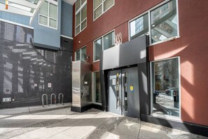 A modern building with a glass facade, a metal entrance gate, and a visible fire alarm panel. - The Eclectic - Open Concept Loft Apartment (Vancouver)