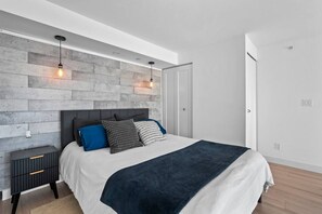 A modern bedroom with a bed, a nightstand, and a wall-mounted light fixture. - The Eclectic - Open Concept Loft Apartment (Vancouver)
