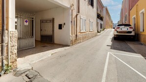 A narrow street with a parked car, a gated entrance, and buildings with shutters. - Apartment 200 Meters From the Beach (Castelsardo)