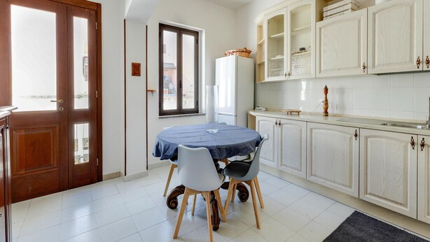 A dining area with a round table, chairs, a refrigerator, and white cabinets. - Apartment 200 Meters From the Beach (Castelsardo)