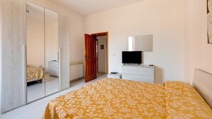 A bedroom with a bed, a wardrobe, a dresser, a television, and a door leading to another room. - Apartment 200 Meters From the Beach (Castelsardo)