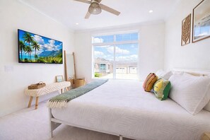 Ein Schlafzimmer mit einem Bett, einem Deckenventilator, einem großen Fenster und Blick auf ein Haus.