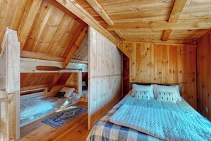 Une cabane en bois avec une chambre à l’étage, un lit superposé et un grand lit avec des oreillers.