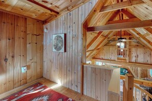 Un intérieur en bois avec un plafond en pente, un tapis rouge à motifs et un tableau encadré au mur.