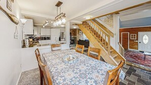 Ein Essbereich mit Tisch, Stühlen, einer Kristallleuchtre und einer Treppe, im Hintergrund eine Küche.