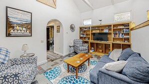 Ein Wohnzimmer mit einer Couch, einem Couchtisch, einem Bücherregal, einem Fernseher und einem gerahmten Bild an der Wand.