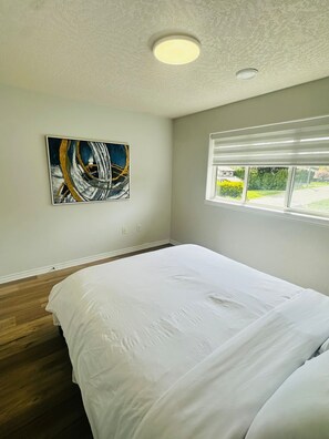 Een slaapkamer met een bed, schilderij, raam en een plafondlamp.