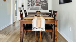 Ein Essbereich mit einem Holztisch, Stühlen, einer gewebten Tischunterlage, einer weißen Tischläufer und einer hängenden Pendelleuchte.