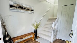 Eine Treppe führt zu einer Tür, eine hölzerne Bank, eine Vase mit Blumen und ein Gemälde an der Wand.