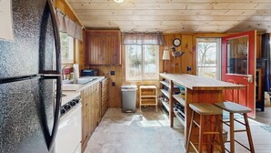 Een compacte keuken met houten kastjes, een koelkast, een spoelbak en een raam.