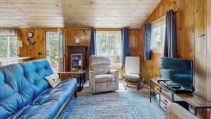 Een houten interieur met een bank, fauteuil, televisie en open haard.