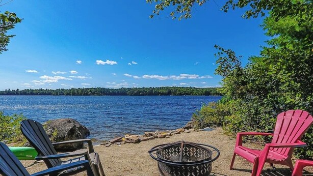 Uitzicht op een meer met Adirondack-stoelen, een vuurplaats en een heldere lucht.