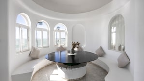 A circular dining table with a black top, surrounded by white seating and arched windows. - Isla Verde 3: Sunset Room in a Tranquil Villa in Cadiz (Copina)