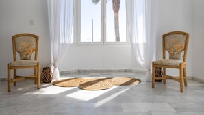 A room with two wicker chairs, a large window with white curtains, and woven mats on the floor. - Isla Verde 3: Sunset Room in a Tranquil Villa in Cadiz (Copina)