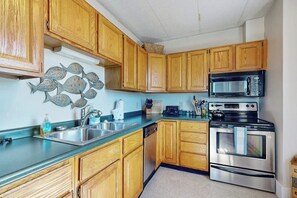 Una cocina con armarios de madera, horno de acero inoxidable, microondas y un lavamanos.