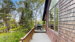 Une terrasse en bois avec un barbecue et du mobilier d’extérieur, entourée d’arbres.