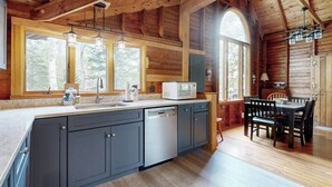 L’intérieur d’une cabane en rondins comprend une cuisine, un coin repas et de grandes fenêtres.