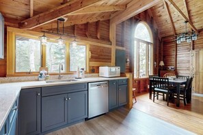 Ein Holzblockhaus-Interieur mit Küche, Essbereich und großen Fenstern.