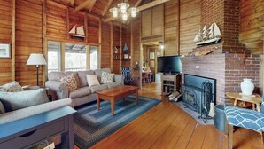 L’intérieur d’un chalet en bois, avec une cheminée, un canapé, un téléviseur et une maquette de bateau posée sur la cheminée.