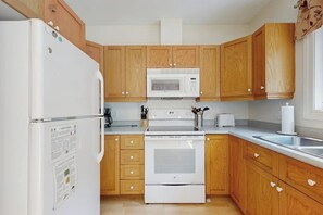 Een keuken met houten kastjes, een witte koelkast, een magnetron, een fornuis en een spoelbak.