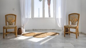 Una habitación con dos sillas de mimbre, un ventanal con cortinas blancas y esteras tejidas en el suelo.