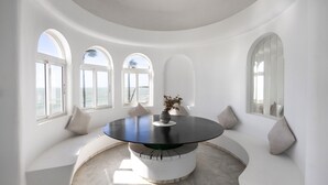 Una mesa circular de comedor con cubierta negra, rodeada de asientos blancos y ventanas arqueadas.