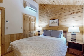 A wooden-paneled room with a bed, two bedside tables, a wall-mounted heater, and a framed picture.