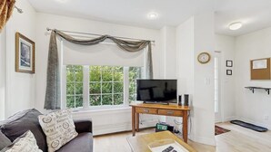 A living room with a TV, sofa, and a window with curtains. - Perfect Cottage Near Downtown & Glen Mary Park w/ Full Kitchen, Free WiFi, More (Bar Harbor)