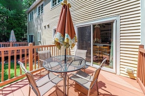 A deck with a glass table and chairs, a patio umbrella, and a wooden fence.