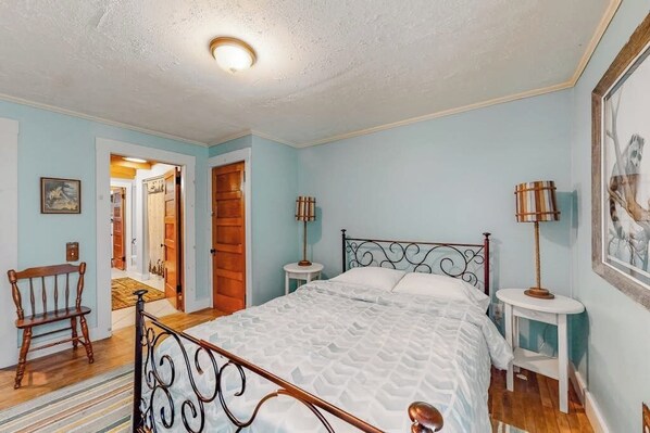 A bedroom with a bed, a chair, two bedside tables, and a door leading to another room. - Lakefront home with outdoor firepit & private dock - near downtown (Greenville)