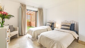 Et hotelværelse med to senge, en sofa, et skrivebord og udsigt til en have.