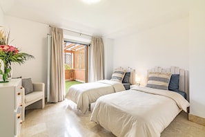 A hotel room with two beds, a sofa, a desk, and a view of a garden. - Waterfront Polo Royale II – Prime Location with Marina Views (Puerto Sotogrande)