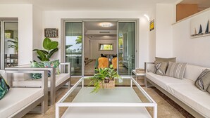 En moderne stue med et glasbord, hvide sofaer og en stor plante.