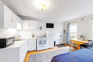 Una cocina compacta con gabinetes blancos, estufa, lavaplatos y un televisor en la pared.