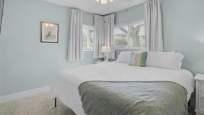 Et soveværelse med en seng, ventilator, et vindue med gardiner og et natbord med lampe.