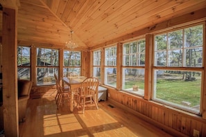 Ein Holzblockbau-Innenraum mit Esstisch, Stühlen, großen Fenstern und einer Chandelier.