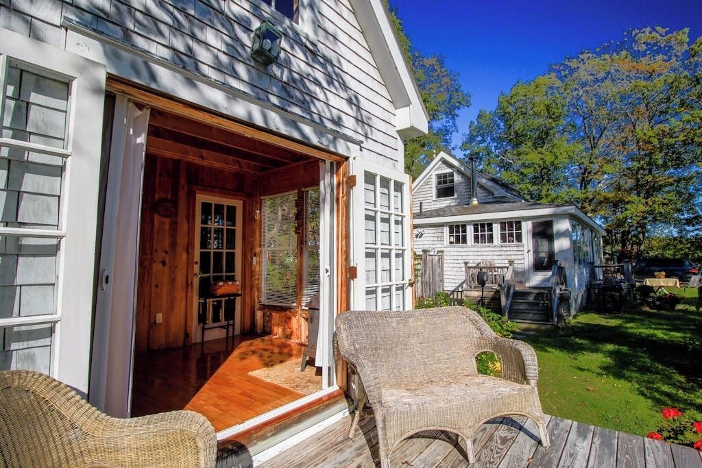 A house with a wooden deck, wicker chairs, and a visible door leading to an interior space.