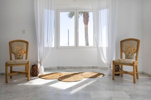 Una habitación con dos sillas de mimbre, un ventanal con cortinas blancas y esteras tejidas en el suelo.