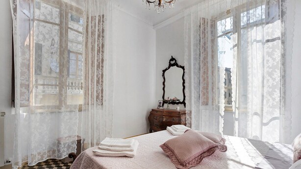 Un dormitorio con suelo a cuadros, una cama con colcha rosa, un aparador y un espejo.