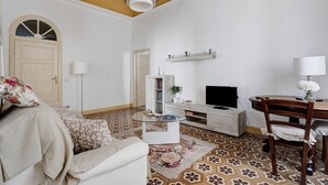 Una sala de estar con un sofá, una mesa de centro, un televisor y un comedor con sillas.