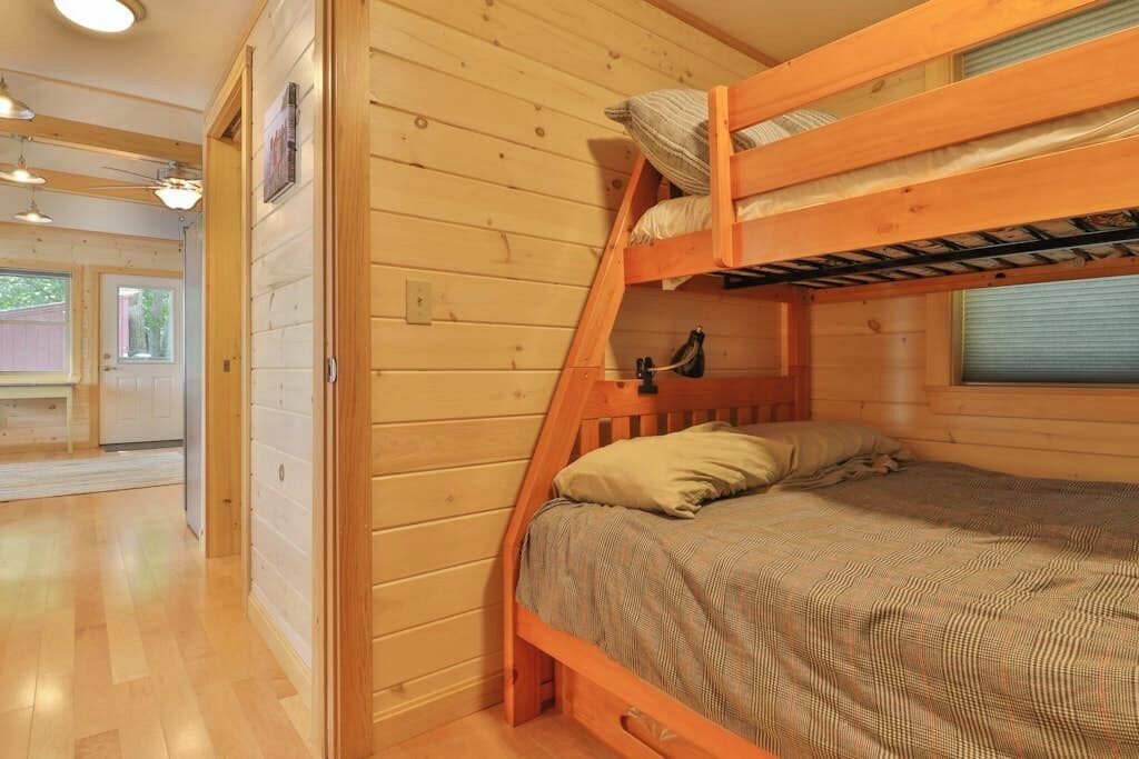Ein Stockbett mit Holzrahmen, ein Einzelbett darunter und ein Fenster mit Jalousien.