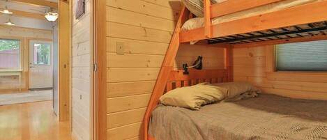 Ein Stockbett mit Holzrahmen, ein Einzelbett darunter und ein Fenster mit Jalousien.