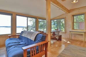 A cabin with a bed, wooden furniture, large windows, and a view of the outdoors.