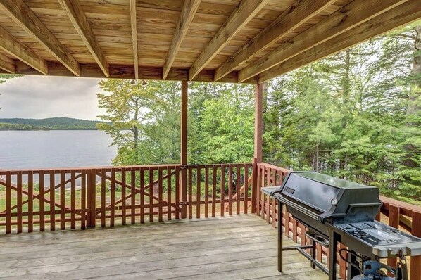 A covered deck with a grill, wooden railings, and a view of a lake and forest. - Lakefront Cabin with Lake Views, Private Dock & Entertainment - Great for Families (Greenville)