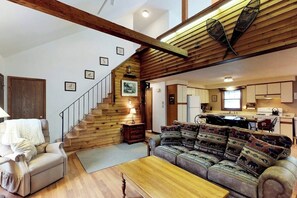 A spacious living room with a wooden staircase, a sofa set, and a kitchen area. - Lakefront Cabin with Lake Views, Private Dock & Entertainment - Great for Families (Greenville)