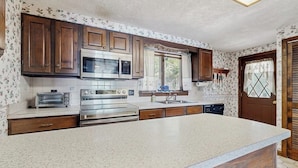 A kitchen with wooden cabinets, a microwave, a toaster, and a dishwasher. - Comfy Lakefront Cabin with Gorgeous Views, Private Dock & Pebble Beach (Lily Bay Township)